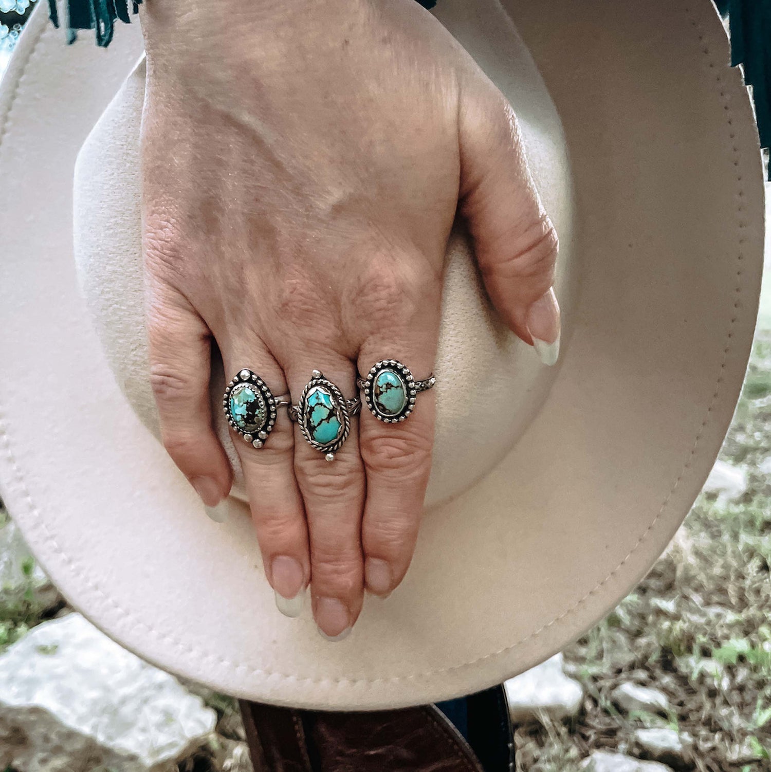 Three oval Golden Hills Turquoise rings on hand holding cream colored western hat.