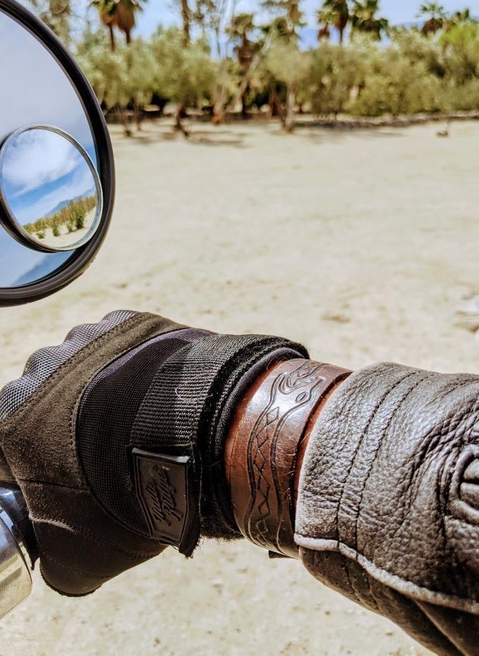 Customer photo wearing brown leather cuff with engraved snake design holding motorcycle handle bars.