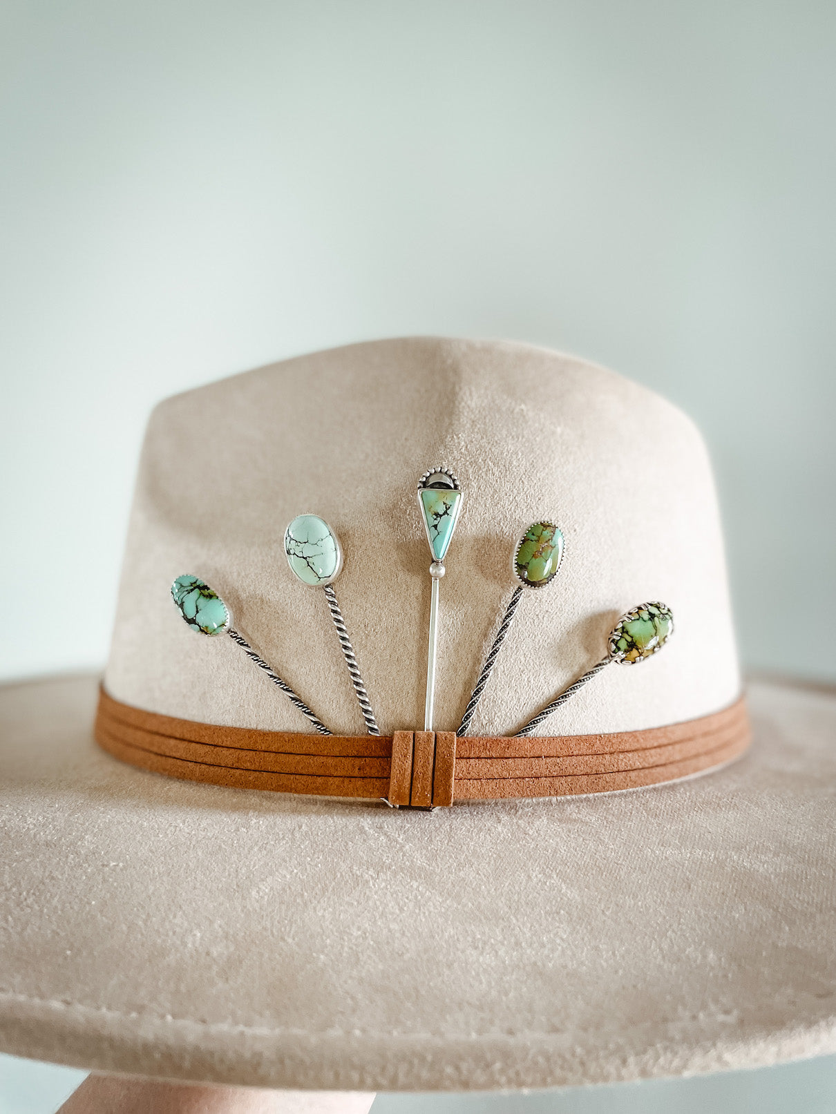Five light blue or green turquoise stick hat pins arranged behind hatband on hat.