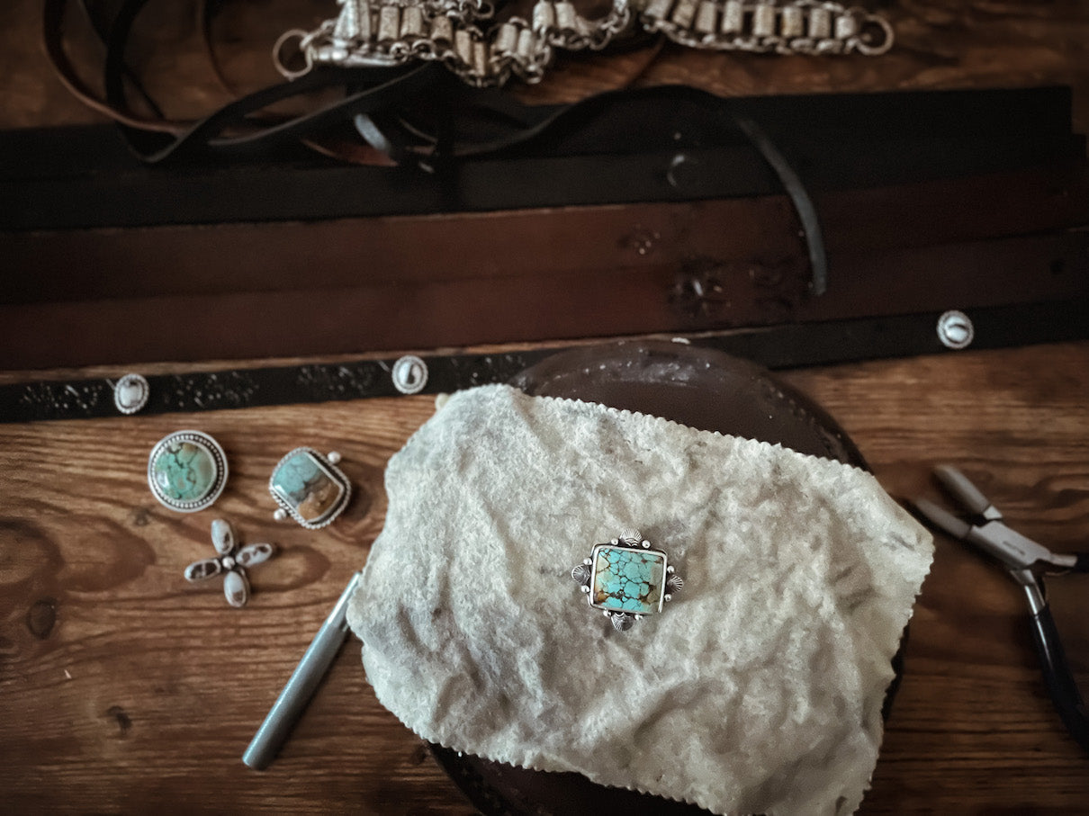 Wood workbench with hatband components, including black and brown leather bands and natural stone sterling silver hat slides, and tools.