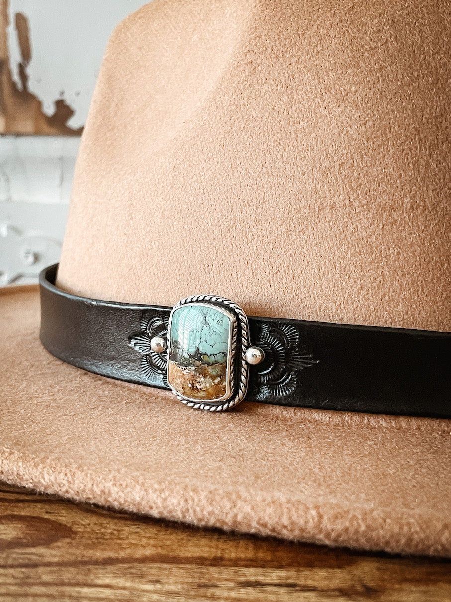 Tan hat with dark leather hatband with stamped design featuring vertical bar shaped blue, brown, and black serpentine stone hat pin set in sterling silver.