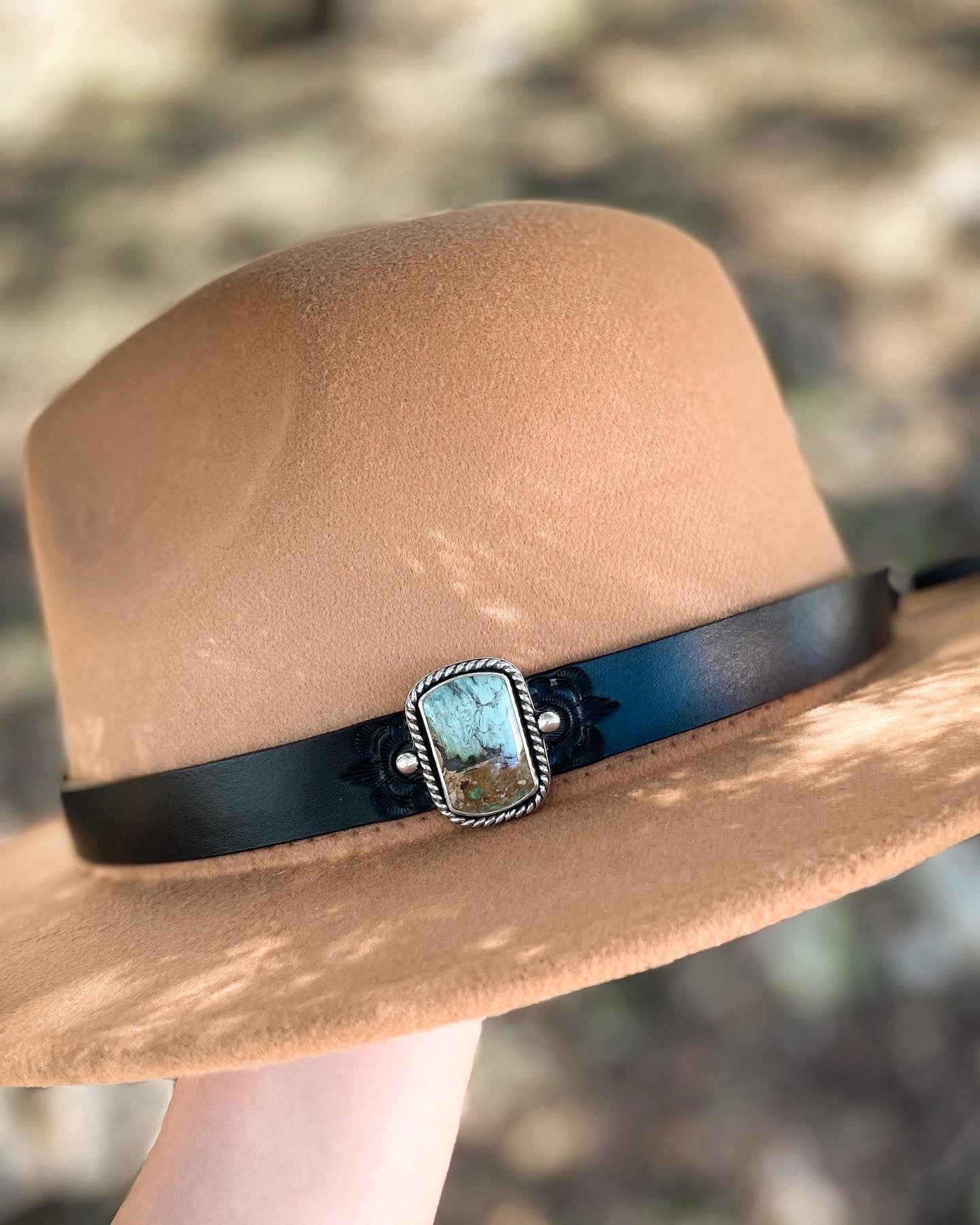 Tan hat with dark leather hatband with stamped design featuring vertical bar shaped blue, brown, and black serpentine stone hat pin set in sterling silver.