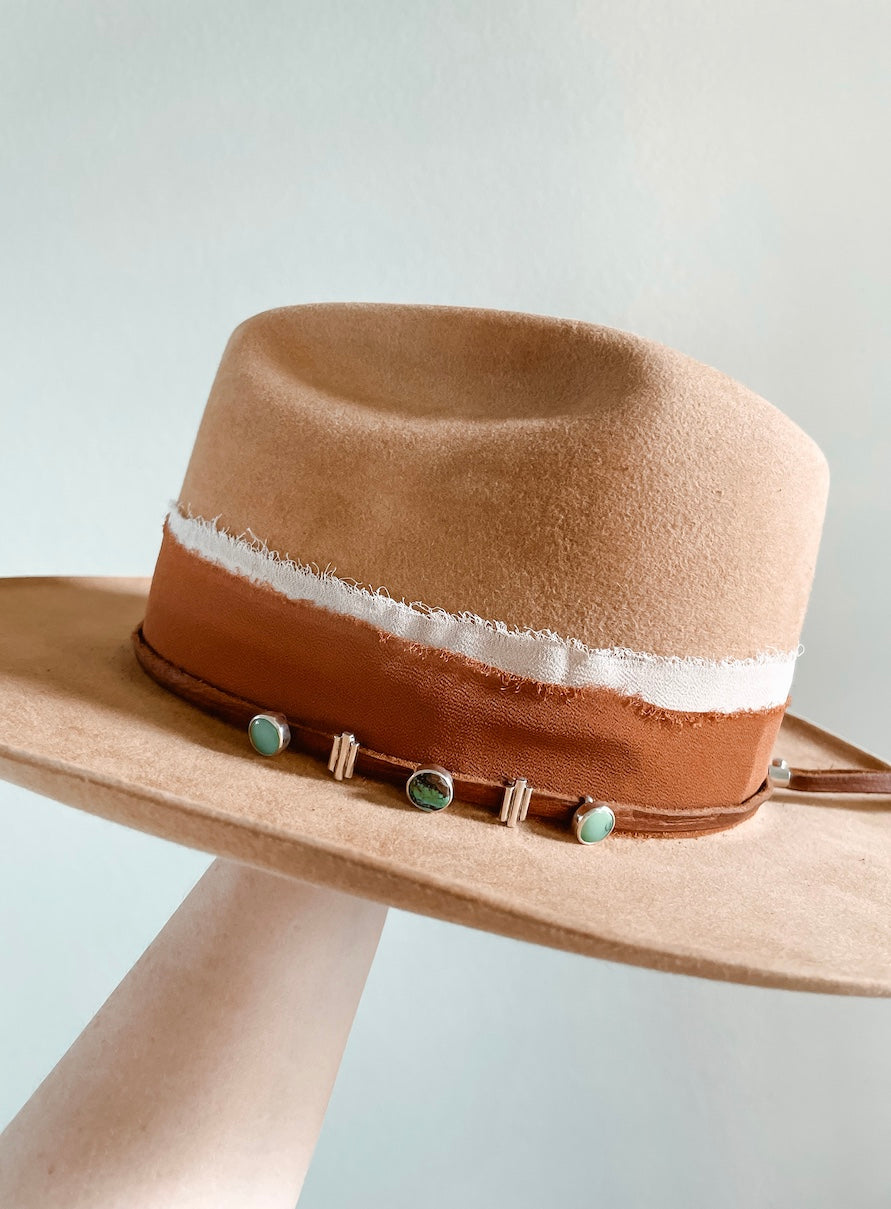 Small turquoise hat slides on hat featuring three round turquoise slides alternating with two silver three vertical bar decorative accent slides on each side on a thin brown leather hat band layered on top of a fabric hatband.