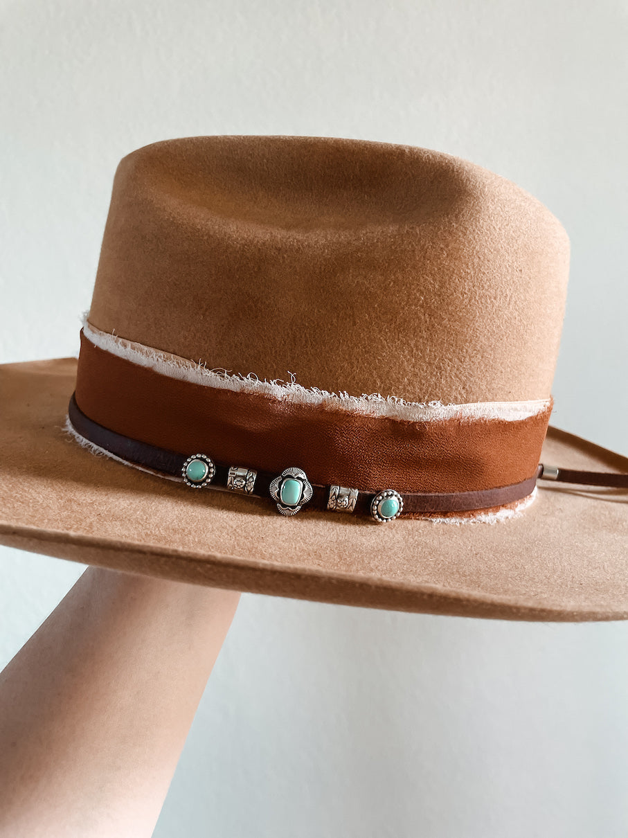 Small turquoise hat slides on hat featuring center cushion stone slide with two silver decorative accent slides on each side and a round stone slide on each end on a thin brown leather hat band layered on top of a fabric hatband.