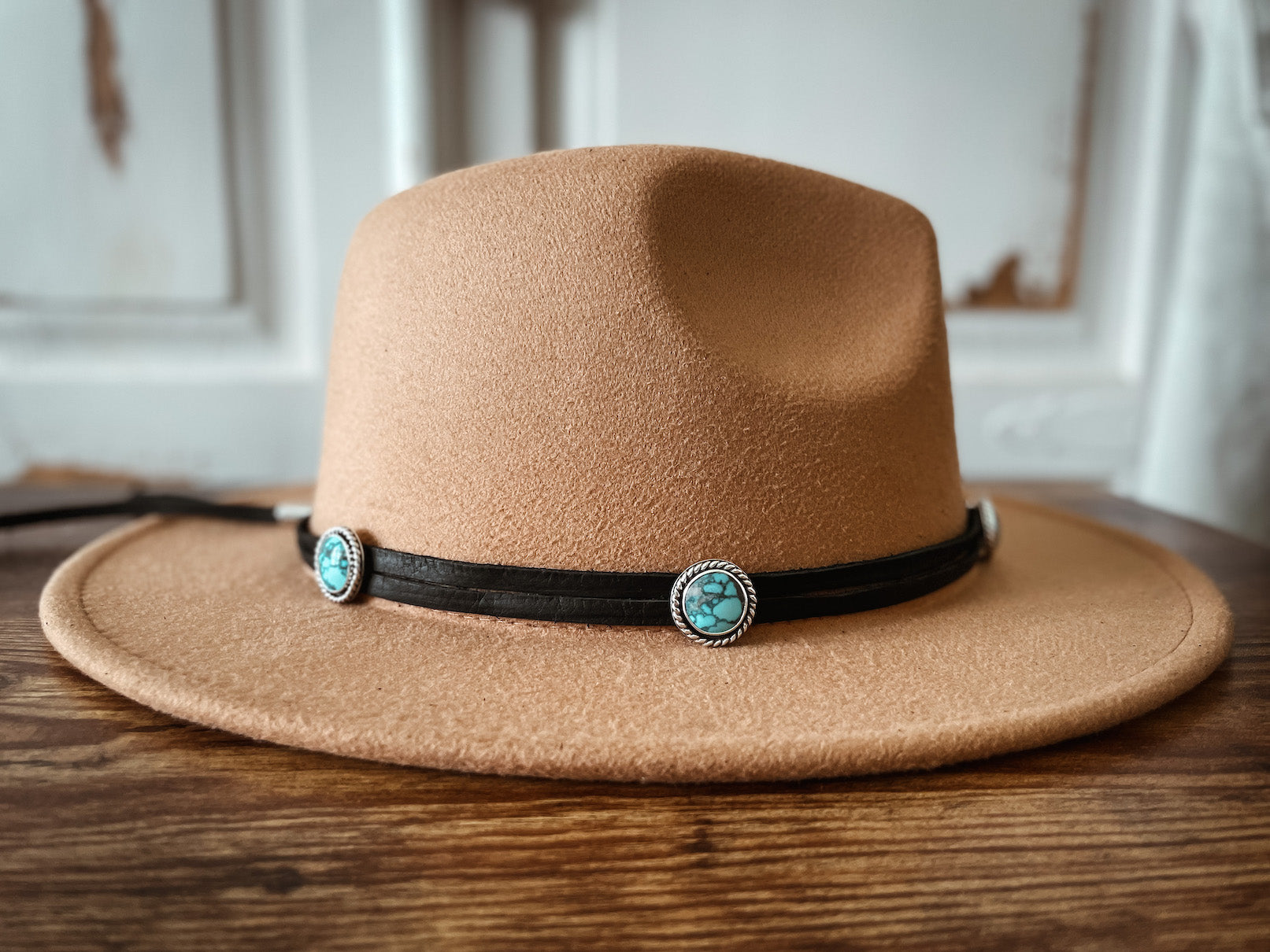 Cream colored hat with dark leather hatband wrap featuring round turquoise stones set in sterling silver.