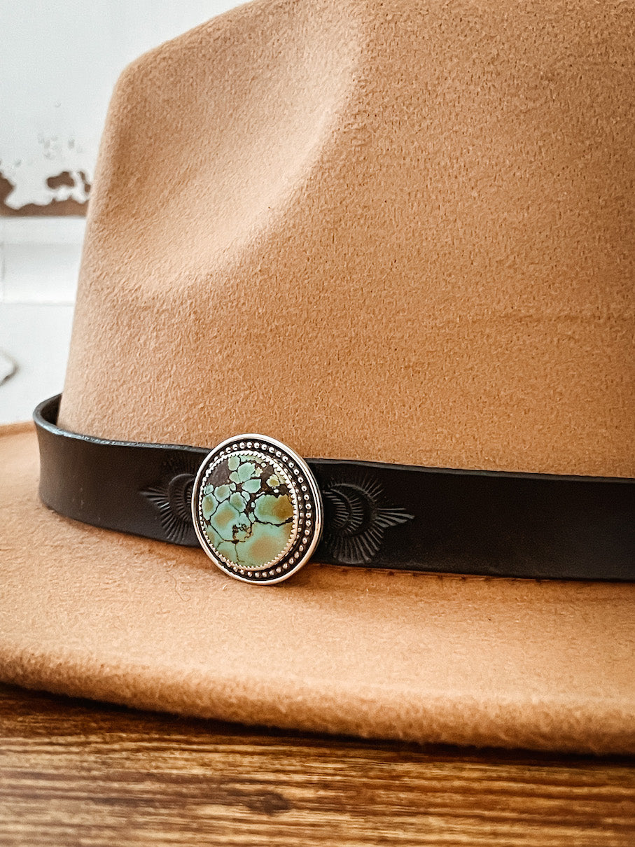 Tan hat with dark leather hatband with stamped design featuring round turquoise hat pin set in sterling silver.