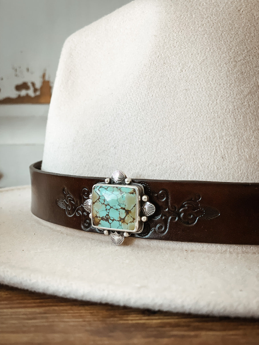 Cream colored hat with dark leather hatband with stamped design featuring square turquoise hat pin set in sterling silver.