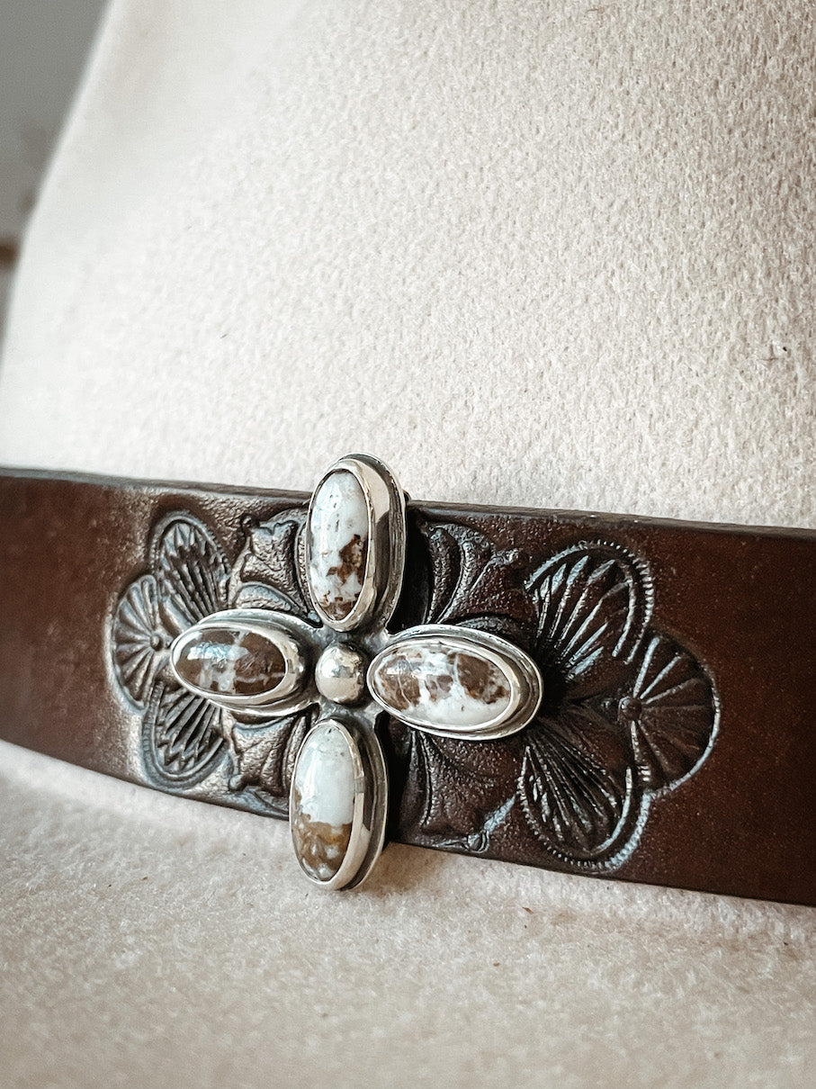Cream colored hat with dark leather hatband with stamped design featuring a hatpin with four oval white buffalo stones set in sterling silver.