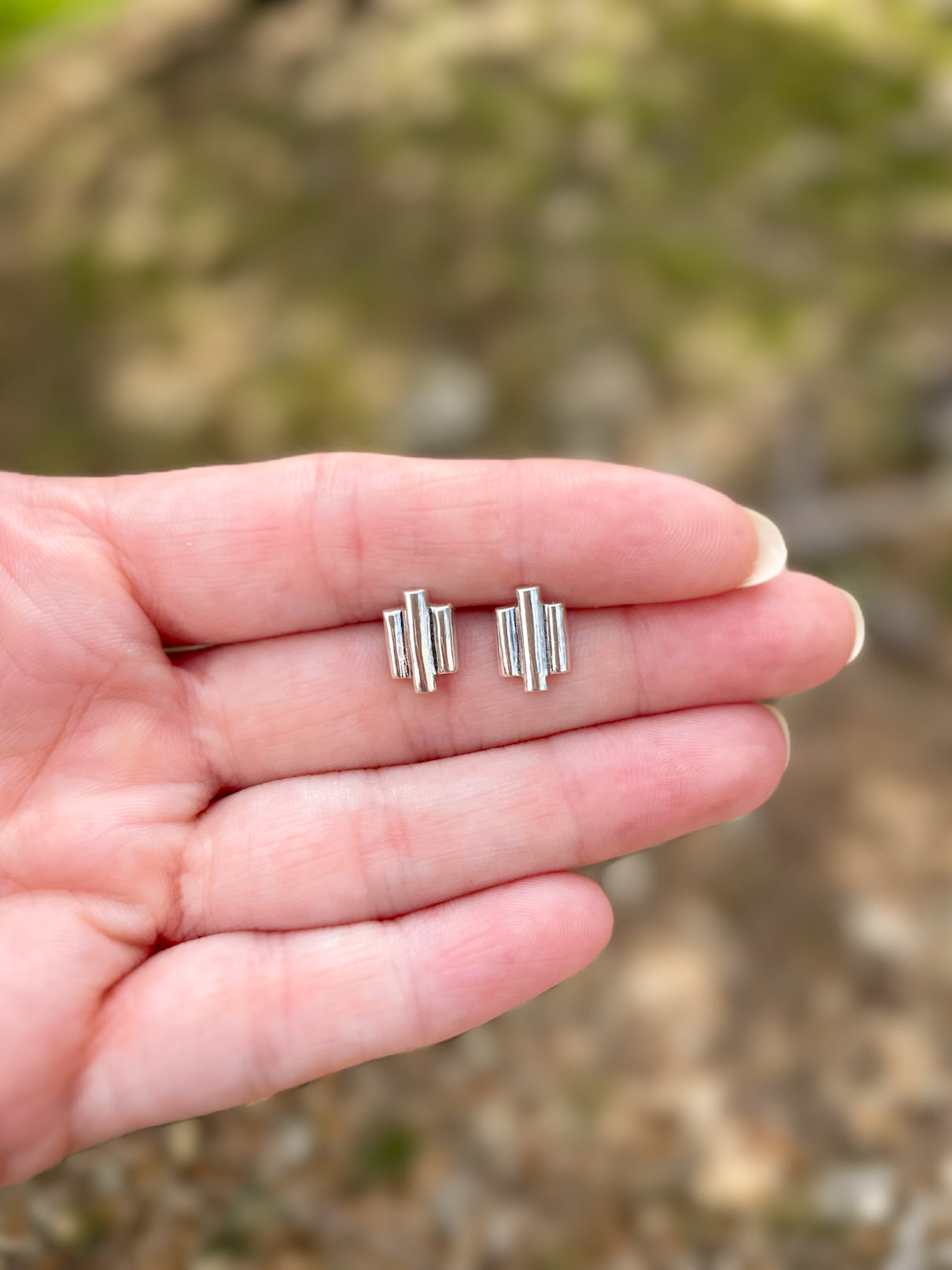 Pair of Art Deco inspired sterling silver 3 bar stud earrings held in hand outdoors in natural light.