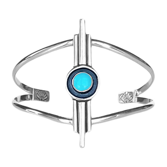 Art Deco inspired sterling silver cuff bracelet. The focal is a 3 bar design with the middle bar slightly longer than the 2 side bars. The middle contains a round turquoise stone encircled with a black patina. The cuff features a double band with stamped accents on the ends.