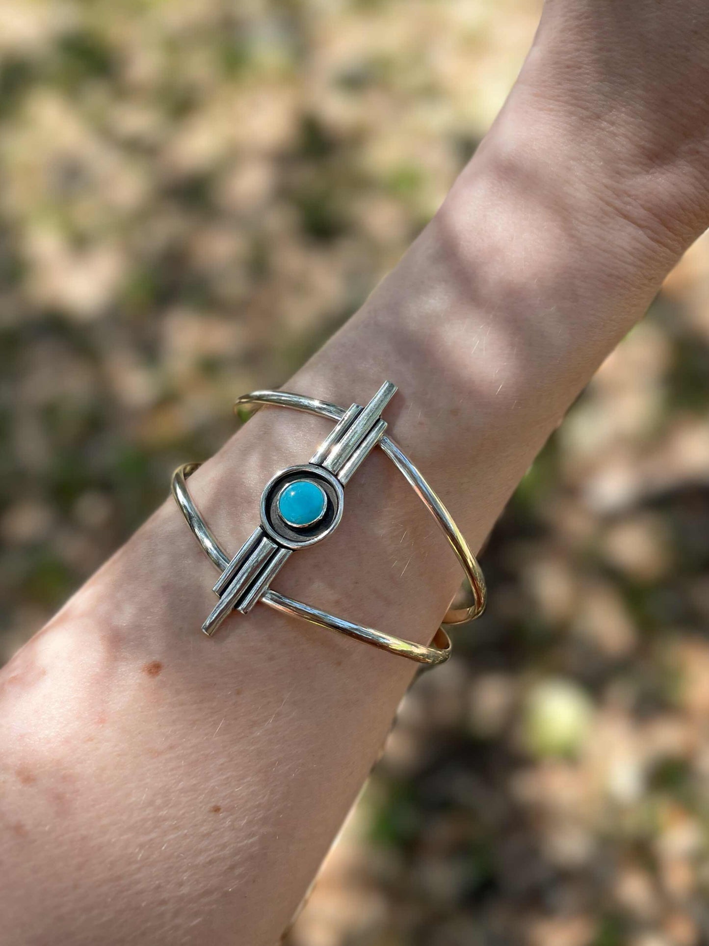 Turquoise Art Deco inspired sterling silver cuff bracelet worn on wrist outdoors in natural light.