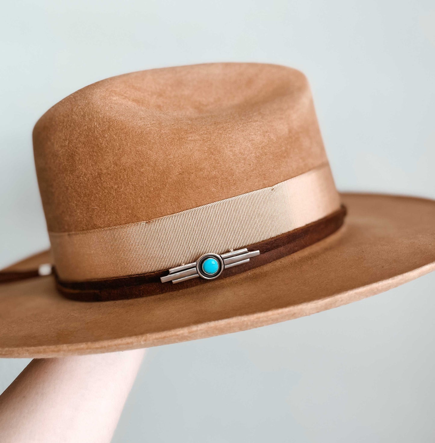 Art deco inspired sterling silver turquoise hat pin on brown leather hat band wrapped around tan hat with cream colored ribbon band. 