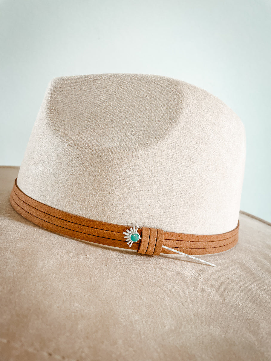 Sterling silver starburst turquoise hat pin in brown leather hat band on cream colored hat.