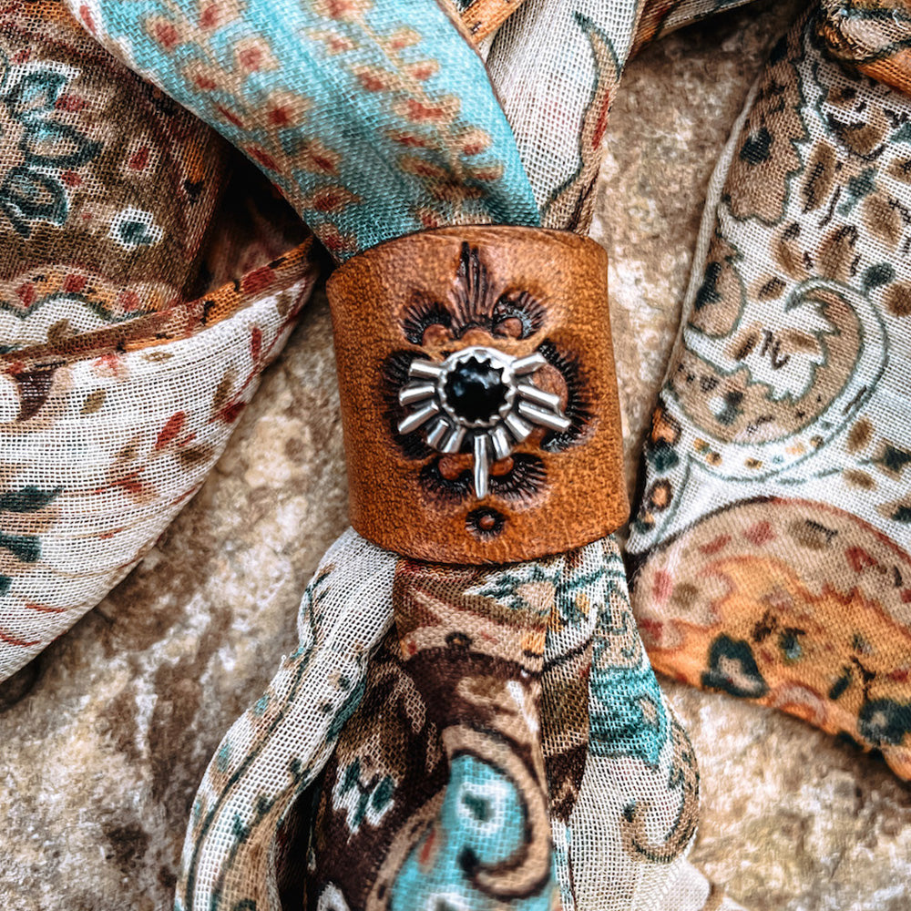 Small round black onyx set in sterling silver with half starburst design on golden tan stamped leather slide on multicolor bandana.