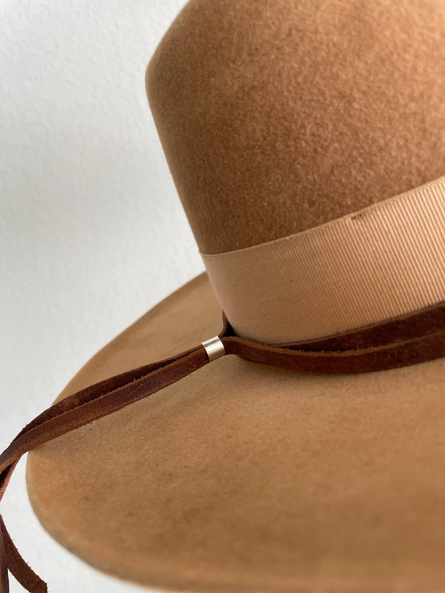 Sterling silver slider on back of brown leather hat band wrapped around tan hat with cream colored ribbon band.