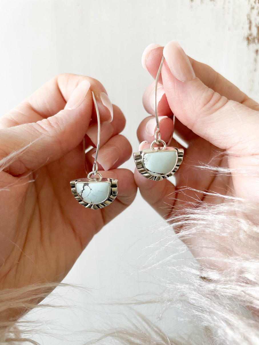 Pair of half moon pale blue turquoise silver dangle earrings held up in hands against white background.