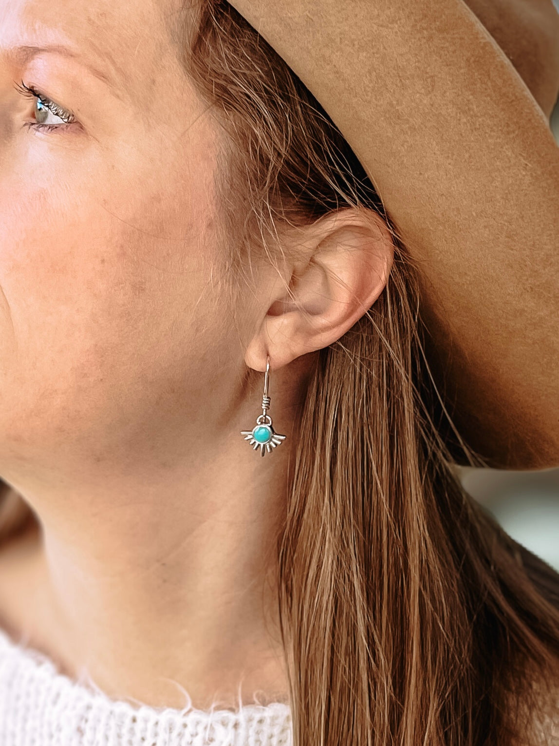 Woman with white sweater and brown hat wearing sterling silver starburst turquoise drop earring in ear.