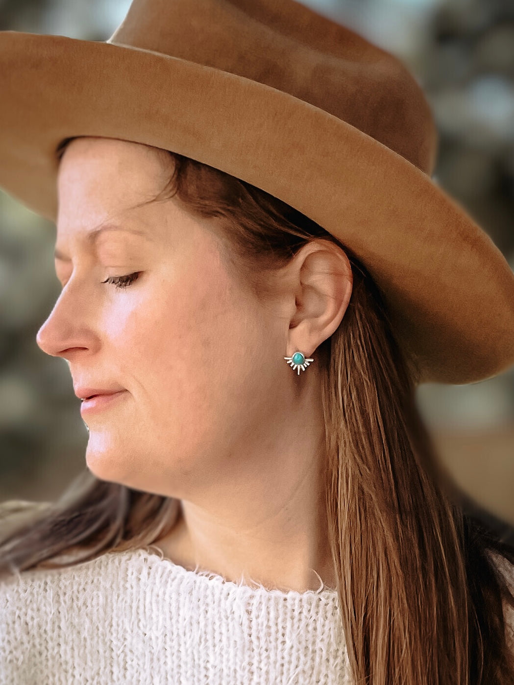 Woman with white sweater and brown hat wearing sterling silver starburst turquoise drop earring in ear.