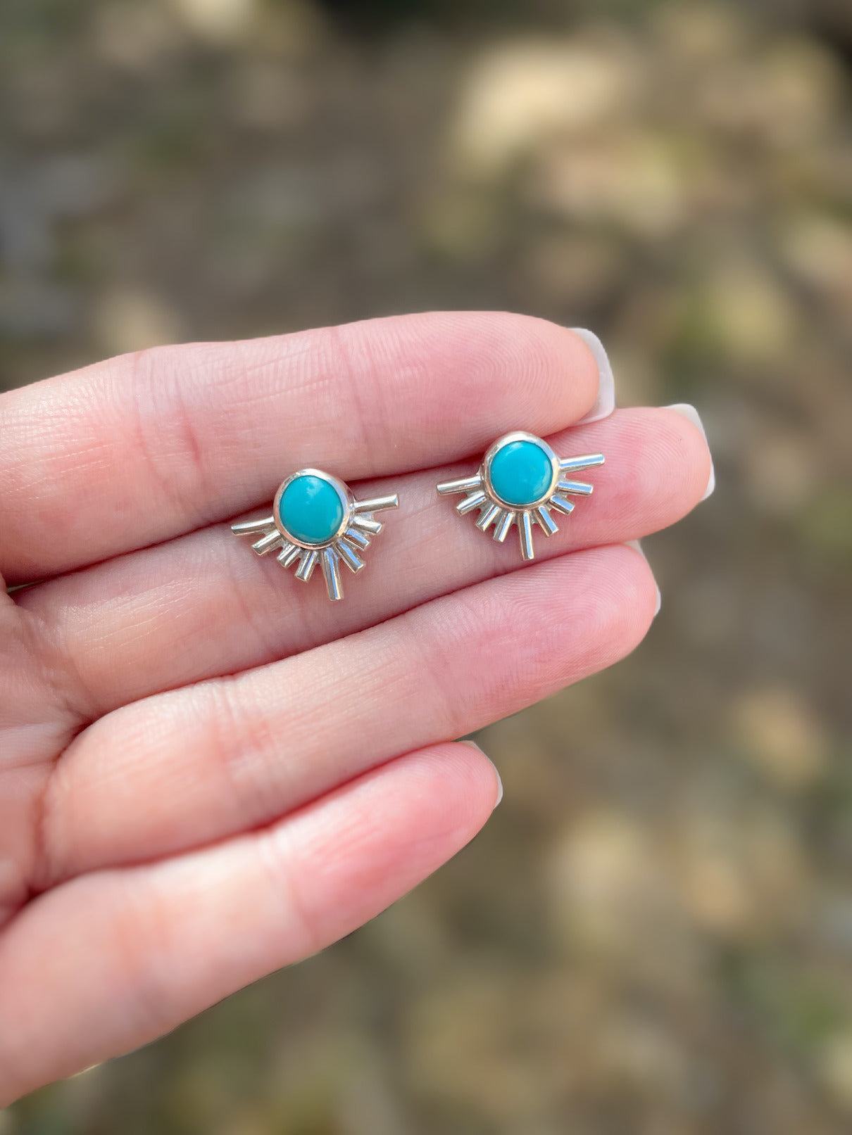 Sterling silver starburst turquoise stud earrings held in hand outdoors in natural light.