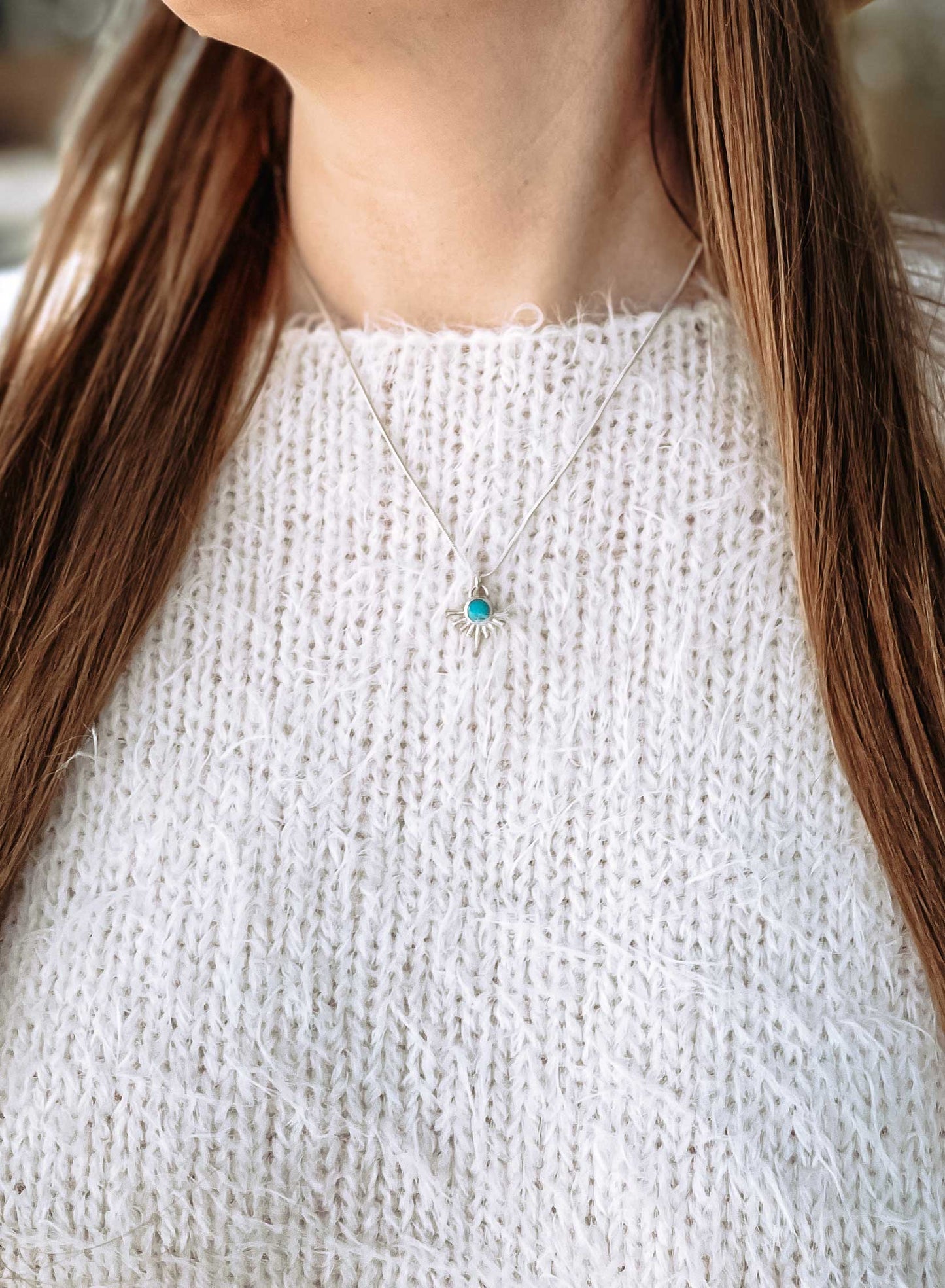 Woman in white sweater outdoors in natural light wearing starburst turquoise necklace on dainty sterling silver snake chain. 