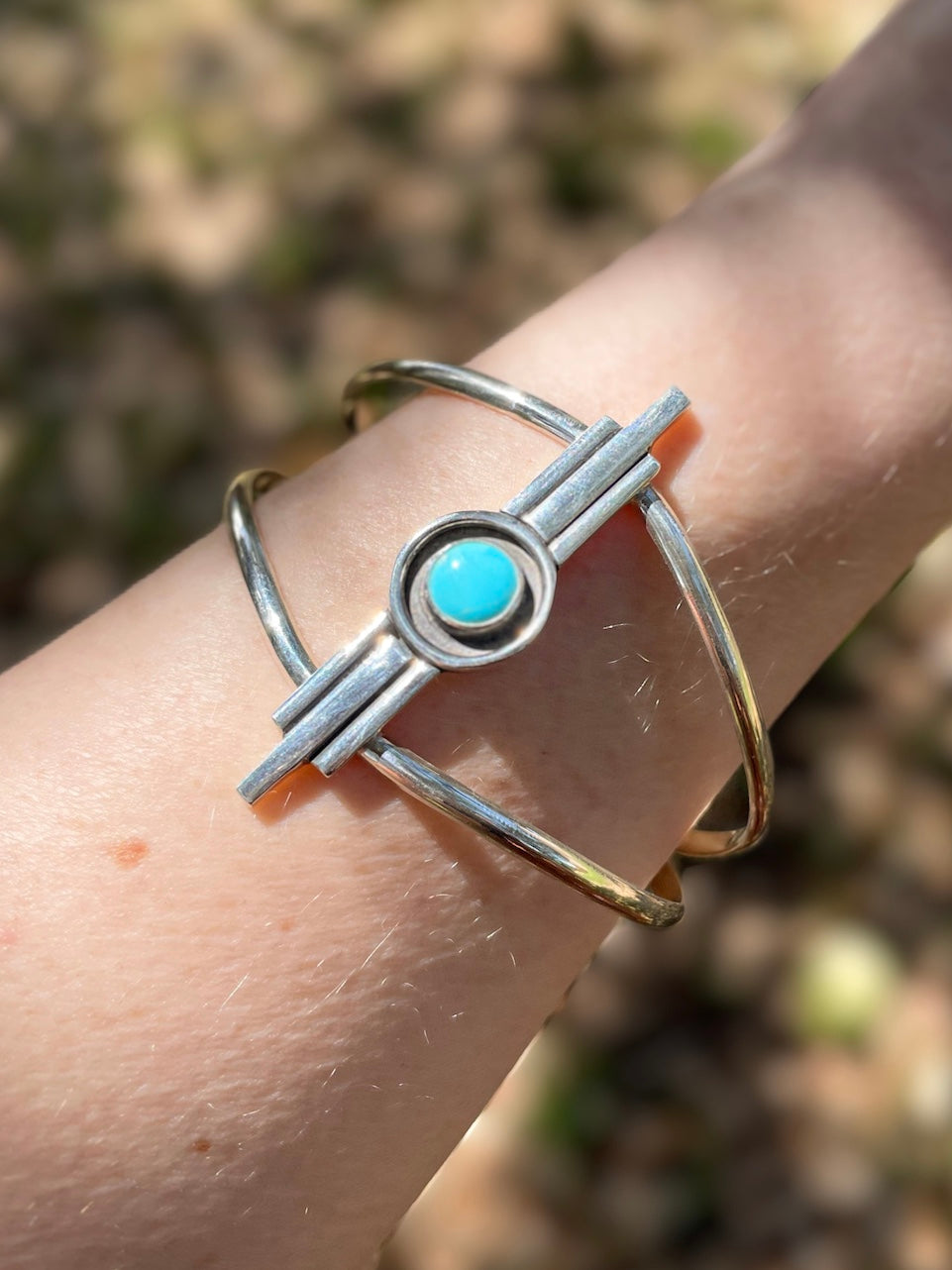 Turquoise Art Deco inspired sterling silver cuff bracelet worn on wrist outdoors in natural light.