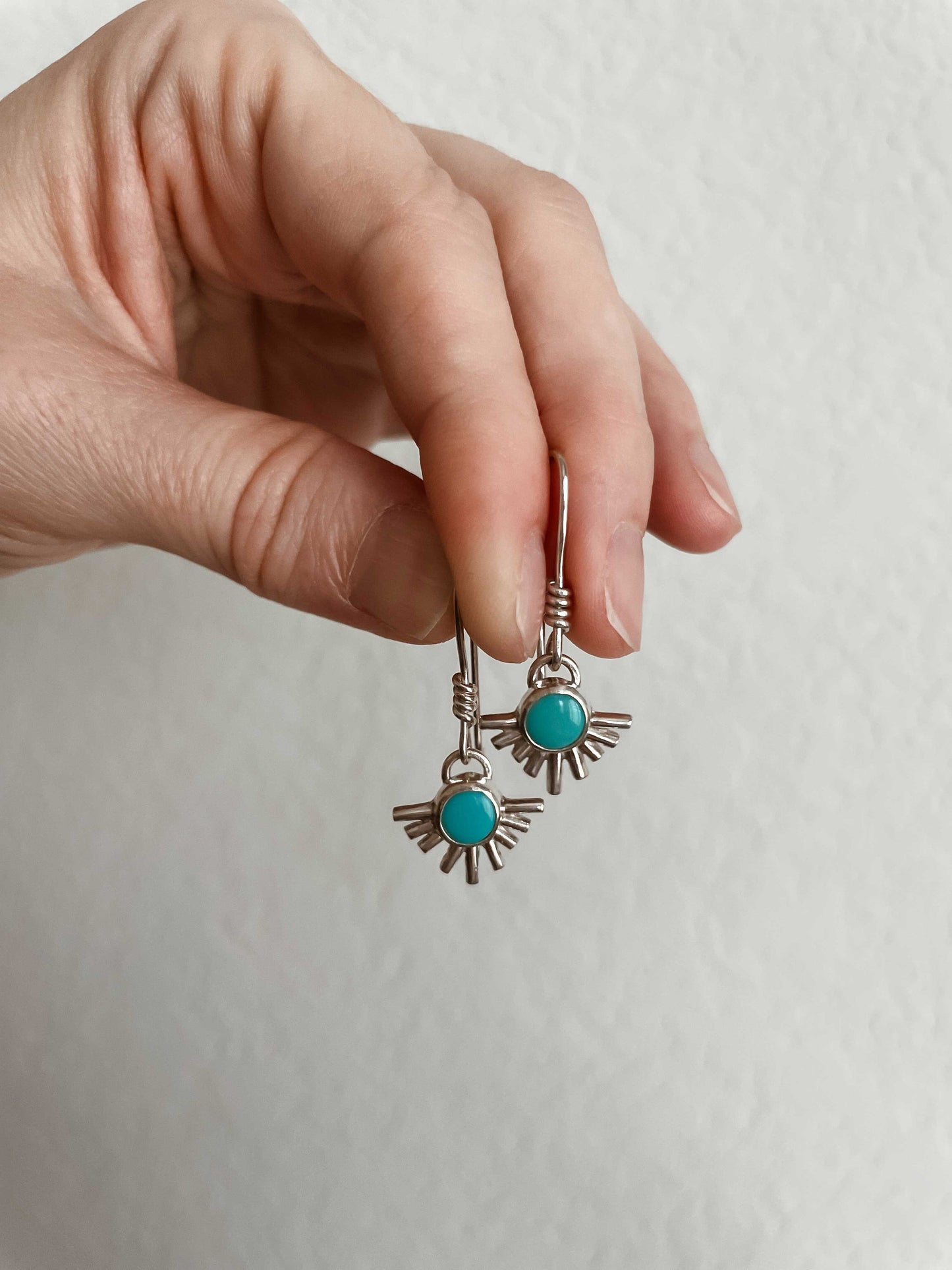 Sterling silver starburst turquoise drop earrings held in hand against white wall.
