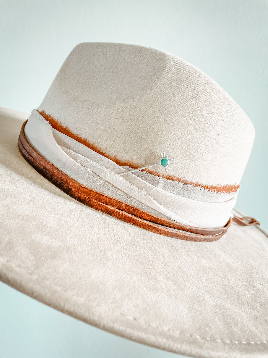 Sterling silver starburst turquoise hat pin in layered brown & cream colored hat bands on cream colored hat.